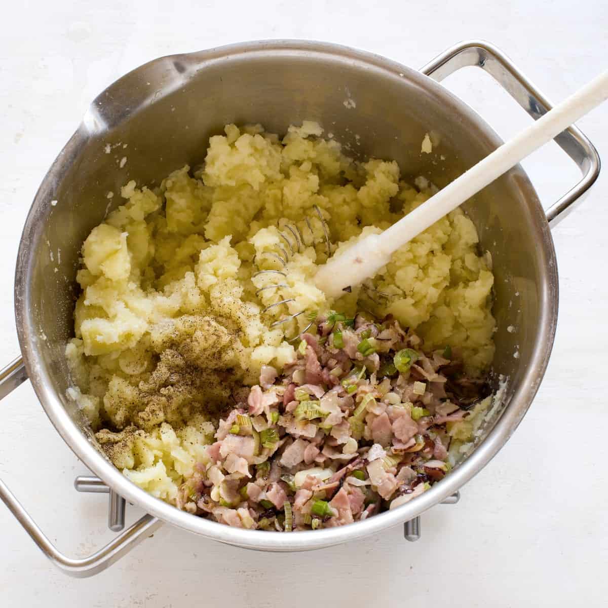 Speck und Zwiebeln zu den zedrückten Kartoffeln zugeben.