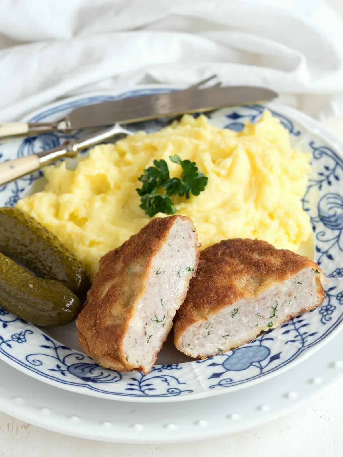 Holländisches Schnitzel serviert mit Kartoffelpüree and Gewürzgurken.