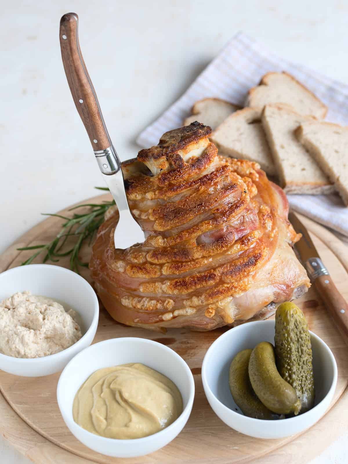 Gebackene Schweinshaxe serviert auf Holzbrett, mit Beilagen.