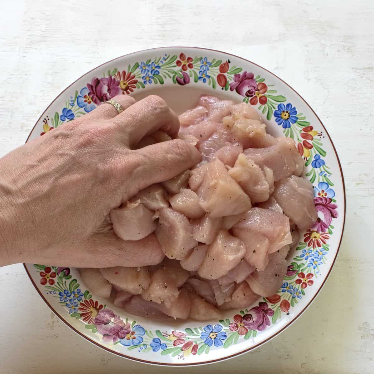 Hähnchenwürfel mit Pfeffer und Salz abschmecken, die Würze mit der Hand einreiben.
