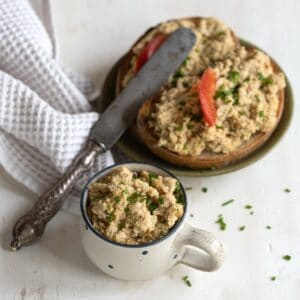 Hefeaufstrich in kleiner Tasse, im Hintergrund zwei Scheiben Brot mit Hefeaufstrich bestrichen.